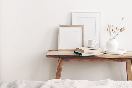Portrait and square wooden picture frames mockups. Vintage bench, table with modern ceramic vase, bunny tail dry grass, books and cup of coffee. White wall background. Scandinavian interior.