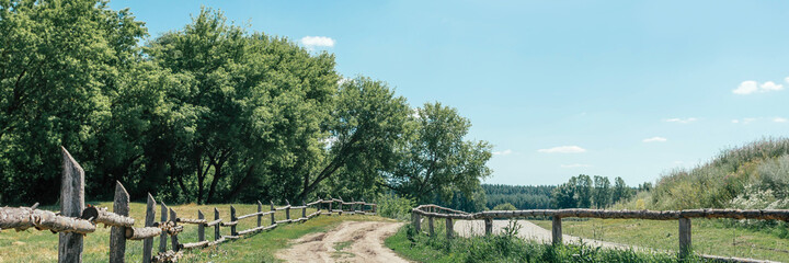 Fototapeta na wymiar Summer countryside landscape. Old wooden fence and country road. Banner.
