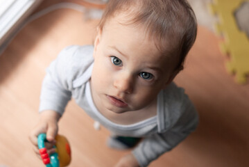 Little boy looks surprised up into the camera. Shooting from above. Child 1 year old boy indoor.