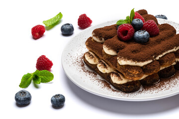 portion of Classic tiramisu dessert with raspberries and blueberries on ceramic plate isolated on white
