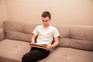 Teenager boy in white T-shirt sits on sofa with laptop