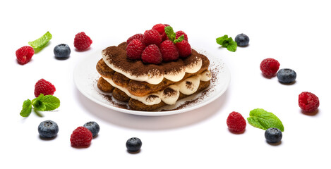 portion of Classic tiramisu dessert with raspberries and blueberries on ceramic plate isolated on white