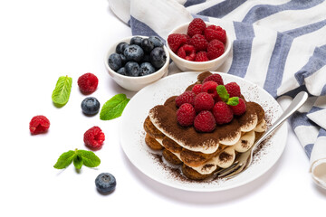 portion of Classic tiramisu dessert with raspberries and blueberries on ceramic plate isolated on white