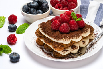 portion of Classic tiramisu dessert with raspberries and blueberries on ceramic plate isolated on white