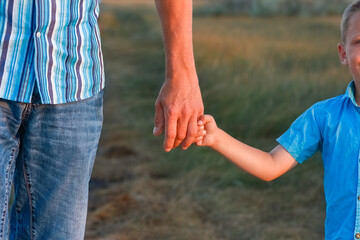 A Hands of a happy child and parent in nature in a park by the road