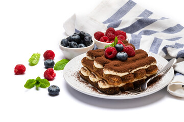 portion of Classic tiramisu dessert with raspberries and blueberries on ceramic plate isolated on white
