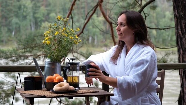 Young Woman in a White Terry Bathrobe Sitting on a Scenic Terrace and Enjoying Breakfast in a Glamping Trip. Cozy Camping, Glamping, Holiday, Traveling, Vacation Lifestyle and Nature concept