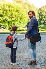 Obraz premium School boy with backpack holding his daddy hand while going to school. Back to school.
