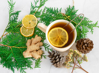 Obraz na płótnie Canvas Drinks for Christmas, Thanksgiving. Tea with lemon and ginger. Autumn, winter drink, hot tea, mulled wine. Christmas tree branches and cones. On a white marble table close-up. View from above