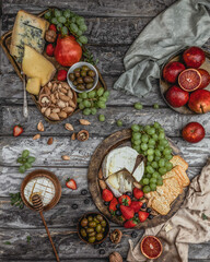 assortment of cheese and fruit on grey wooden background with nuts, berries and textile, wine appetizer, top view