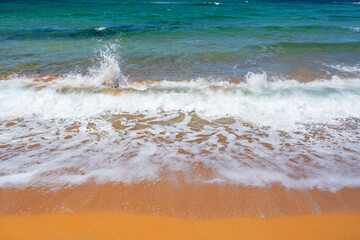 Waves on a beach with orange sand and blue water