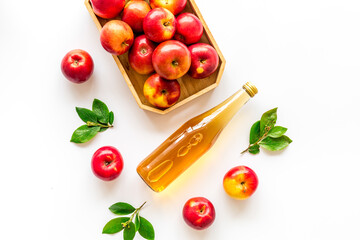 Apple cider vinegar in glass bottle and wooden tray with red apples