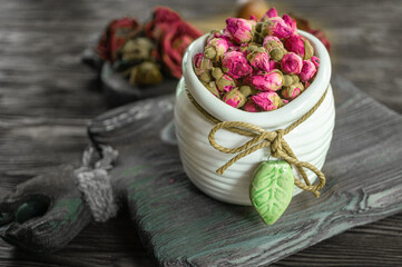 Flower tea rose buds in a white vase on an old wooden table. Close up