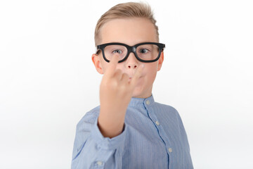 Young Caucasian boy in glasses,blue shirt and shows hands with rock gesture.Studio portrait,white wall.