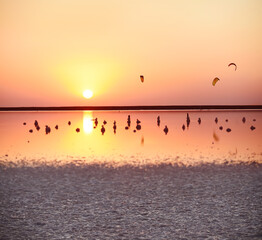 Sunset on the pink lake. Columns in crystals of salt in water and kitesurfers against the setting sun.
