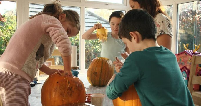 Family with young children carving jack o' lanterns made out of pumpkins. Halloween background in slow motion
