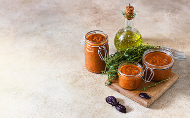 Delicious vegetable caviar in jars, thyme and purple basil on wooden board, light stone background. Homemade caviar with eggplant, tomatoes and bell pepper. Copy space.
