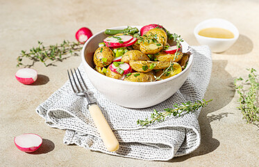 Homemade potato salad with green beans, fresh radishes and herbs dressing with olive oil and mustard sauce, light concrete background. Bright sunlight and trendy shadows.