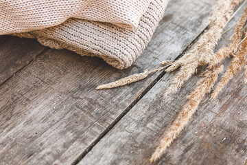 Autumn or winter background. Stack of cozy knitted wool clothes sweaters and dried plant on wooden table. Hygge mood, cold weather concept. Handmade knitted sweaters.