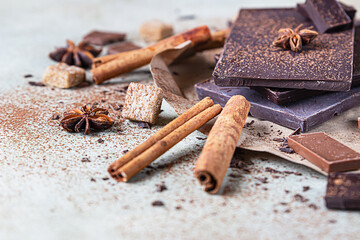 Dark and milk chocolate chunks, cocoa powder, cinnamon, anise star and brown sugar on stone background. Confectionery shop advertising and cooking ingredients concept.