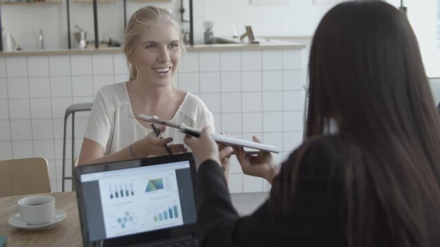 Young female customer taking agreement from financial advisor, signing paper, giving it back and shaking hands. Medium shot. Contract or deal concept