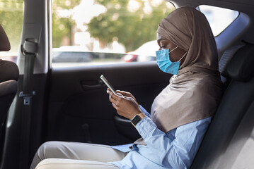 Black muslim businesswoman in hijab wearing medical mask on backseat of car