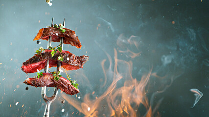 Close-up of tasty beef steak on black fork, fire flames in foreground