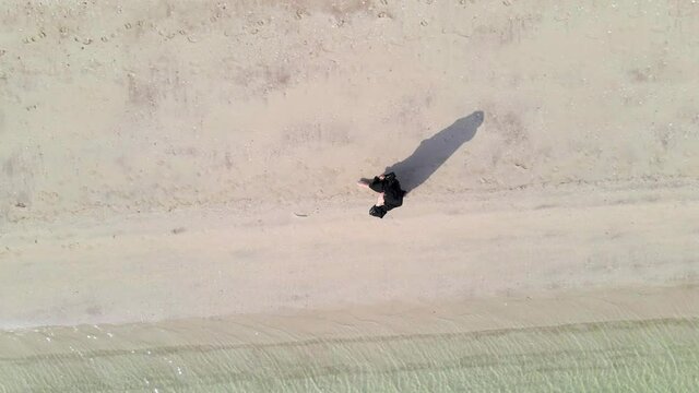 Muslim woman walking by the seaside wearing hijab abaya dress aerial view