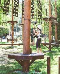 Brave little girl in the forest adventure park, wearing helmet and safety equipment at amusement center for children outdoor 