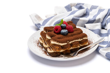 portion of Classic tiramisu dessert with raspberries and blueberries on ceramic plate isolated on white background with clipping path
