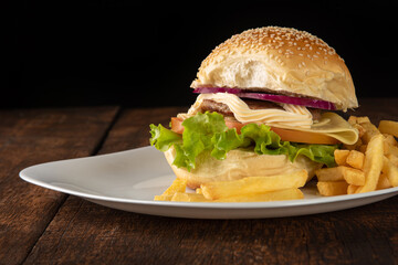Hamburger and French fries placed on a white plate on rustic wood with black background, selective focus.