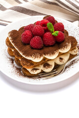 portion of Classic tiramisu dessert with raspberries on ceramic plate isolated on white background with clipping path