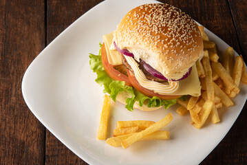 Hamburger and French fries placed on a white plate on rustic wood with black background, selective focus.
