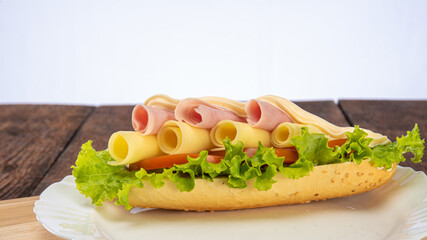 Sandwich of mayonnaise, cheese, ham, tomato and lettuce placed on a white plate on a rustic wooden table, selective focus.