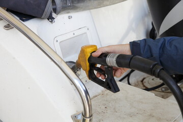 Captain hand with yellow fuel gun in motor boat fuel filler socket on gas station, watercraft...