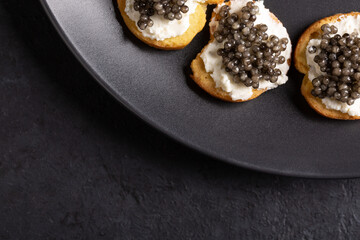 Sandwiches with black caviar on black slate background. Top view, close-up, copy space.