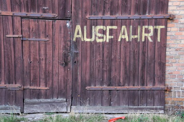 verwittertes, hölzernes, rorbraunes GAragentor mit gemalter Aufschrift "Ausfahrt"