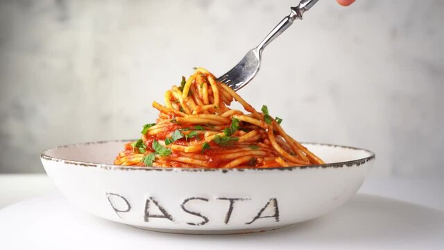Close up of a fork taking spaghetti with tomato sauce from the plate