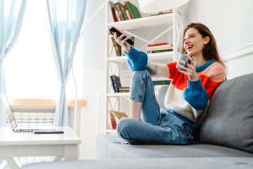Photo of girl drinking coffee and using remote control while watching tv