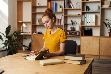 Image of thinking redhead girl reading book while sitting at table