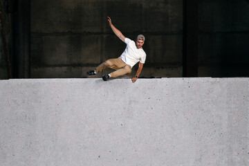 Young strong parkour and freerunning athlete jumping over the wall in urban environment. Copy...