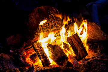 A roaring camp fire burns at a camp site, nearby wood has been collected and stacked in the pile, burning for many hours in to the night.