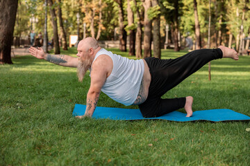 Fat caucasian bearded and bold man with tattoos is doing yoga exercses to loose his weight
