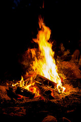 A roaring camp fire burns at a camp site, nearby wood has been collected and stacked in the pile, burning for many hours in to the night.