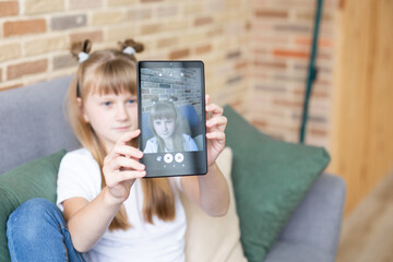 Teenage schoolgirl doing homework with digital tablet at home. A child using gadgets to study. Education and distance learning of children. Homeschooling during quarantine. Stay home fun.