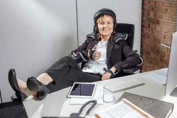 Thumbs up: Young female employee at work in the office, wearing a helmet and protectors to ward off...