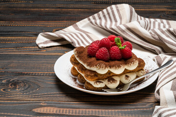 portion of Classic tiramisu dessert with raspberries on ceramic plate isolated on wooden background