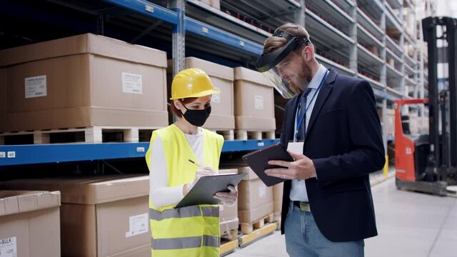 Woman worker and man manager with gloves and face mask talking in warehouse, coronavirus concept.