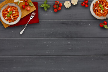 A banner image depicting 2 bowls of delicious tomato pasta in a rustic bowls, garnished with a sprig of basil, with ingredients, on a dark wooden background with copy space