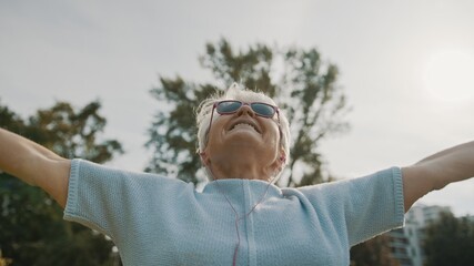 Cool grandmother with pink sunglasses and headphones stretching in the park. Recreation in old age.low angle. High quality photo